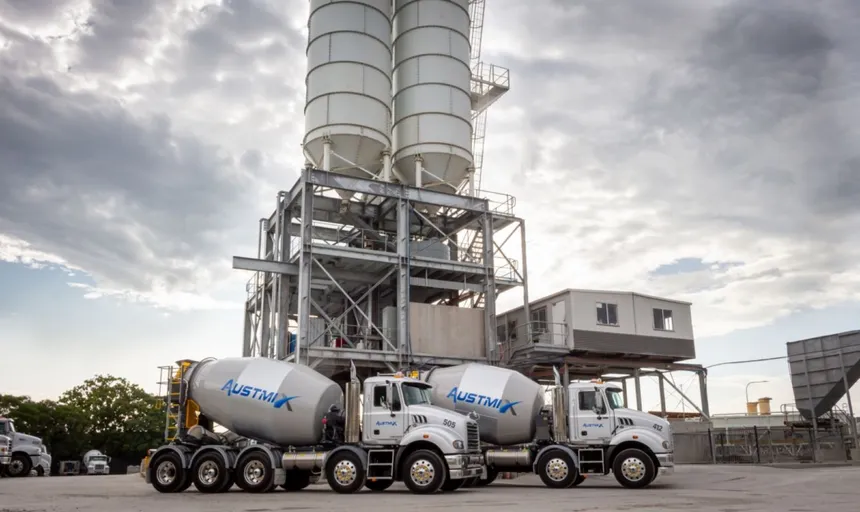 Two Cesco mixer trucks beneath cement silos at a batching plant