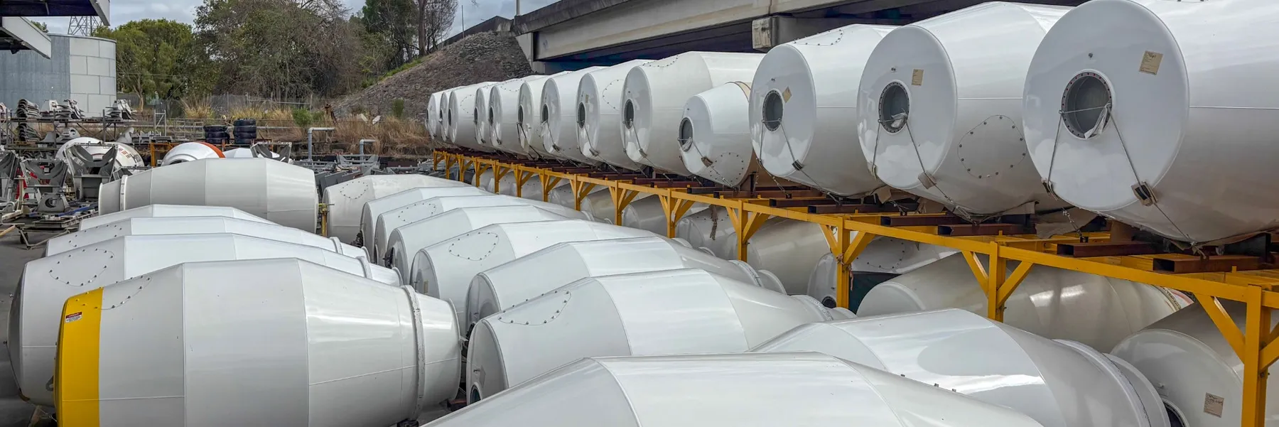 Rows of new white Cesco mixer barrels, some stacked on yellow racks