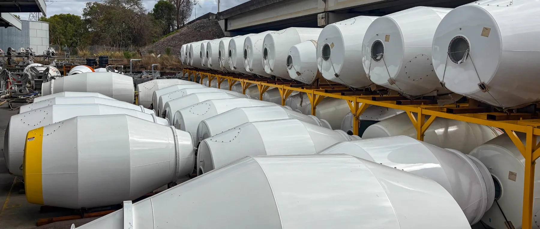 Rows of new white Cesco mixer barrels, some stacked on yellow racks