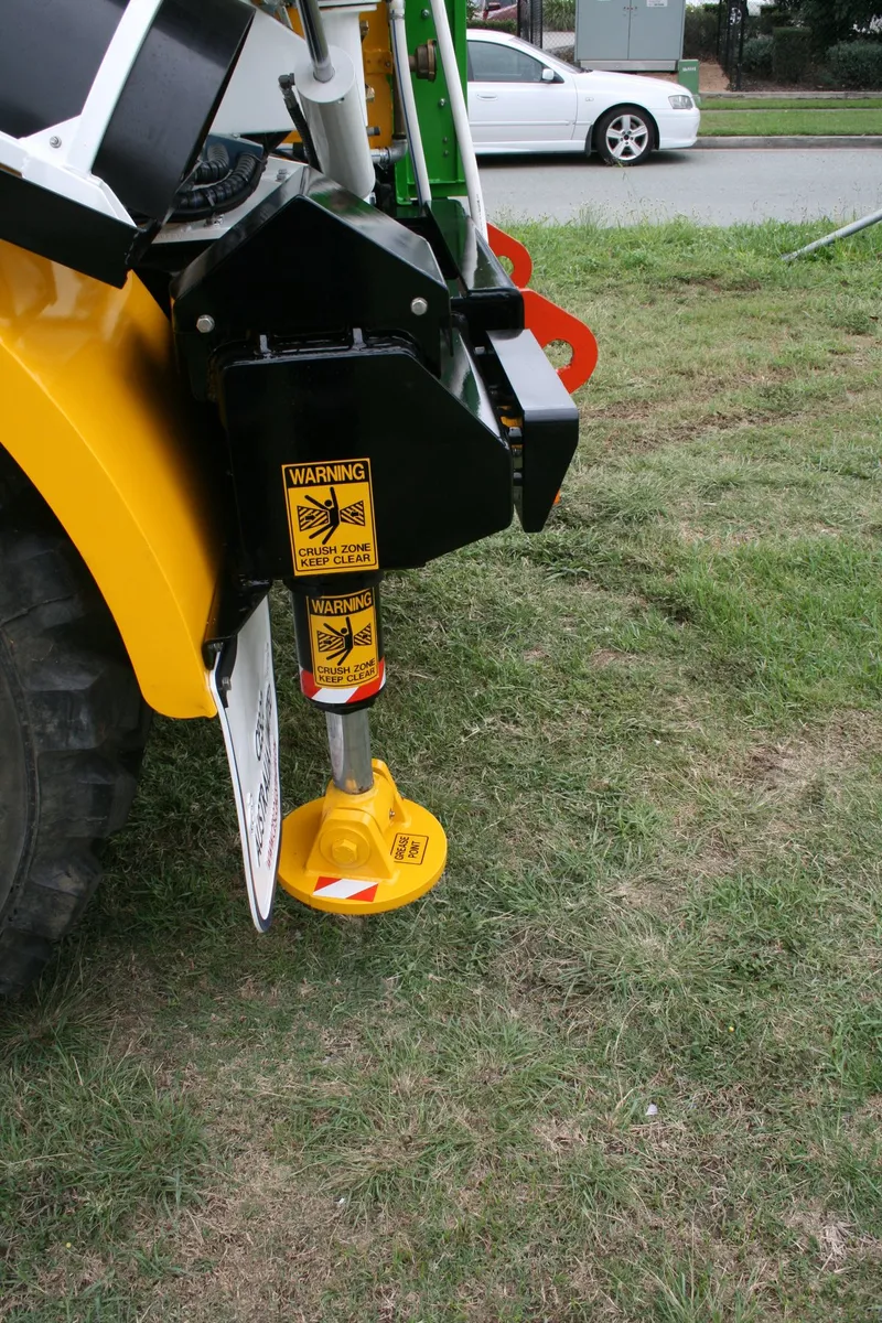 Rear hydraulic stabiliser leg with crush-zone warning labels on the mining mixer