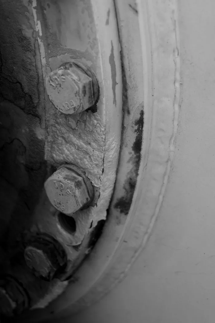 Corroded bolts and peeling paint around the gearbox mount ring on a mixer barrel dished end