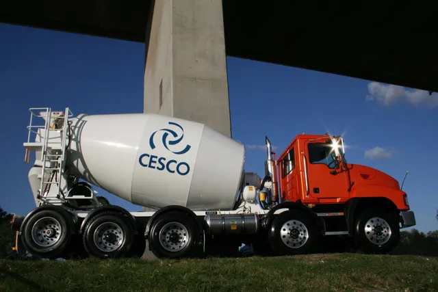 Orange Mack truck with white Cesco mixer bowl under a freeway overpass
