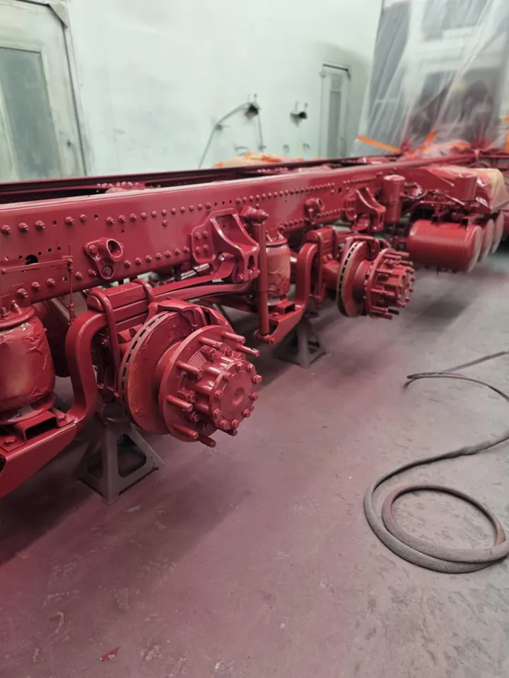 A truck chassis freshly painted in deep red, with axles and hubs refinished