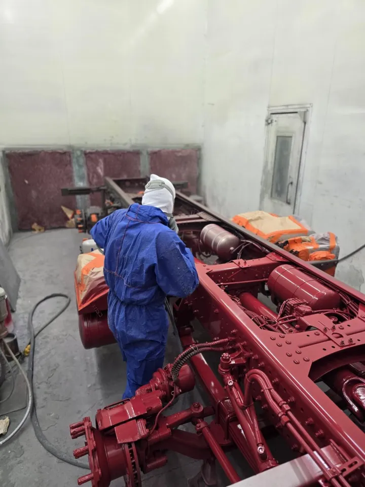 A painter in protective overalls spraying a truck chassis in the paint booth